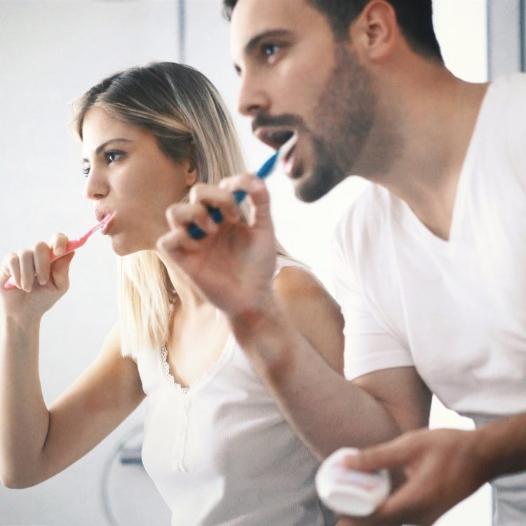 Male and Female Brushing Their Teeth Together While Looking In The Mirror